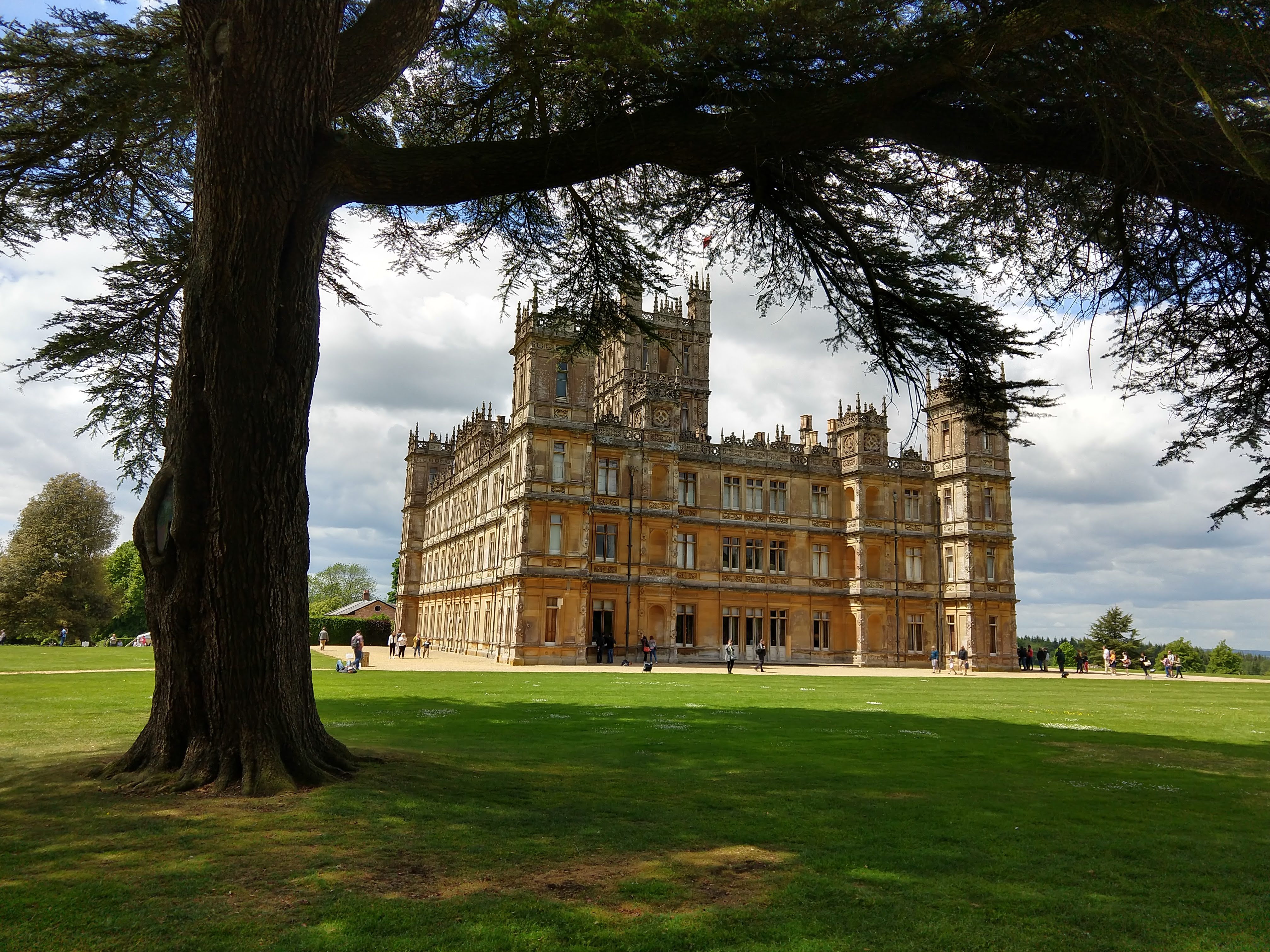 Highclere Castle seen across the lawn beneath a large tree